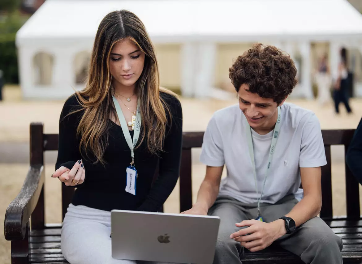 Two students, a boy and a girl, are sitting reading something on a laptop.