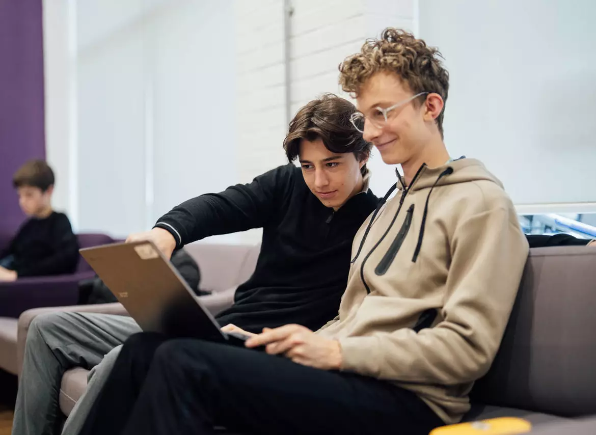 Two students are sitting on the couch with a laptop, discussing rolling decisions.