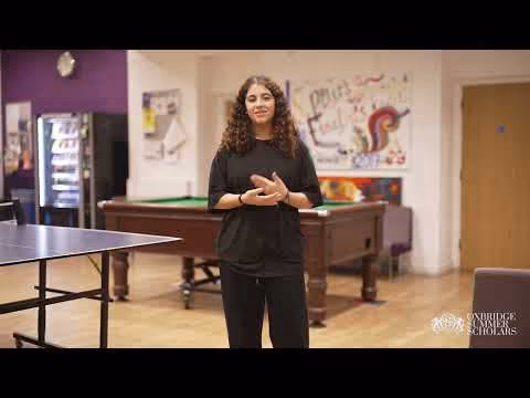 Young woman with curly hair standing and smiling in a recreational room with a pool table and a ping pong table.