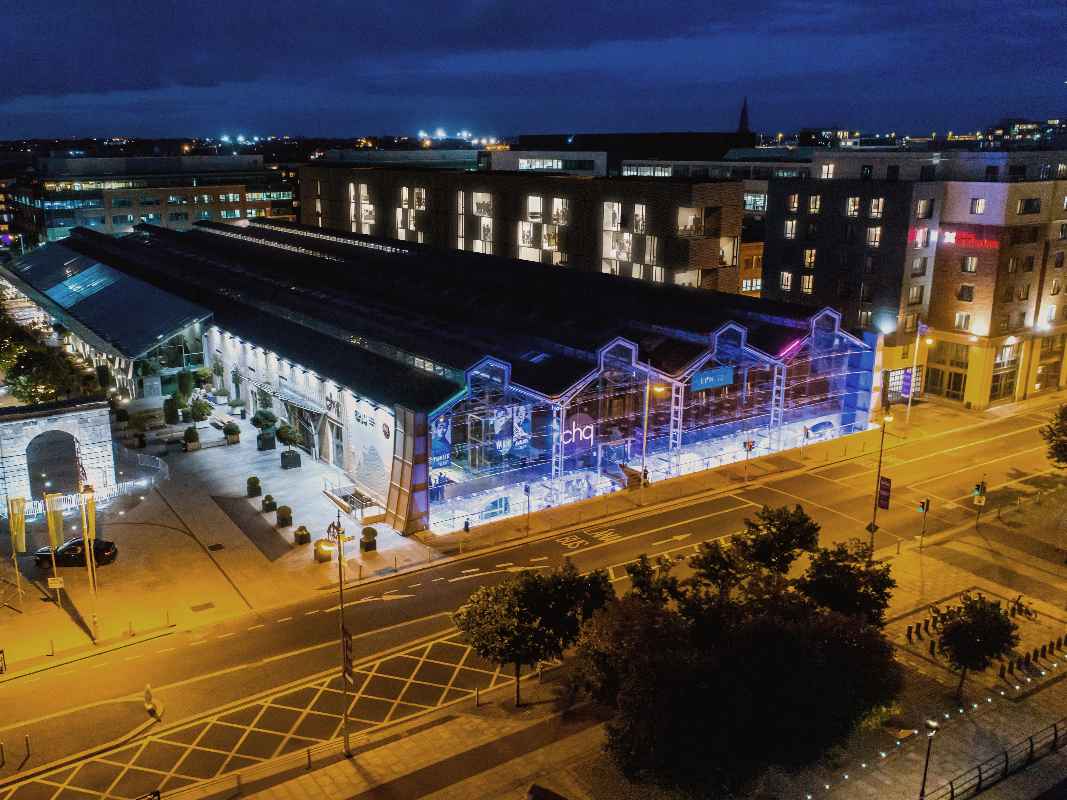 Bright living room with large windows, white sofas, wooden coffee table, and several green indoor plants.
