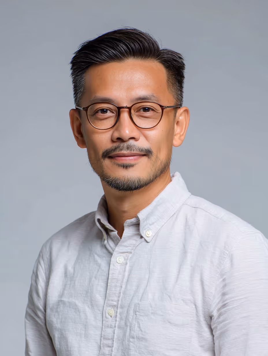 Middle-aged man with short black hair, glasses, and a trimmed beard wearing a white button-up shirt against a gray background.