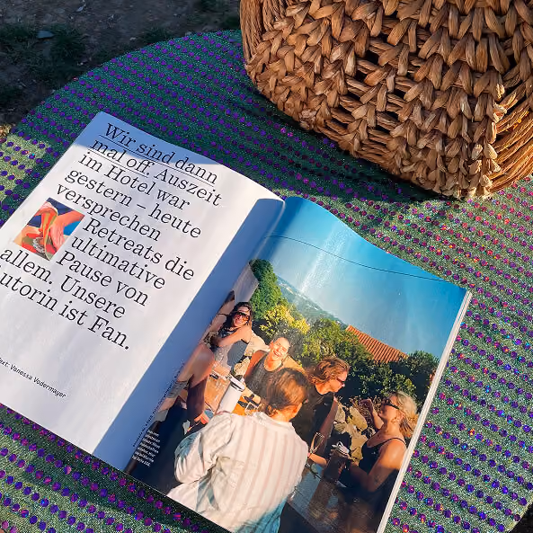 Offenes Magazin mit Foto von Menschen bei einem Treffen draußen auf einem Tisch mit bunter Decke und Korb.