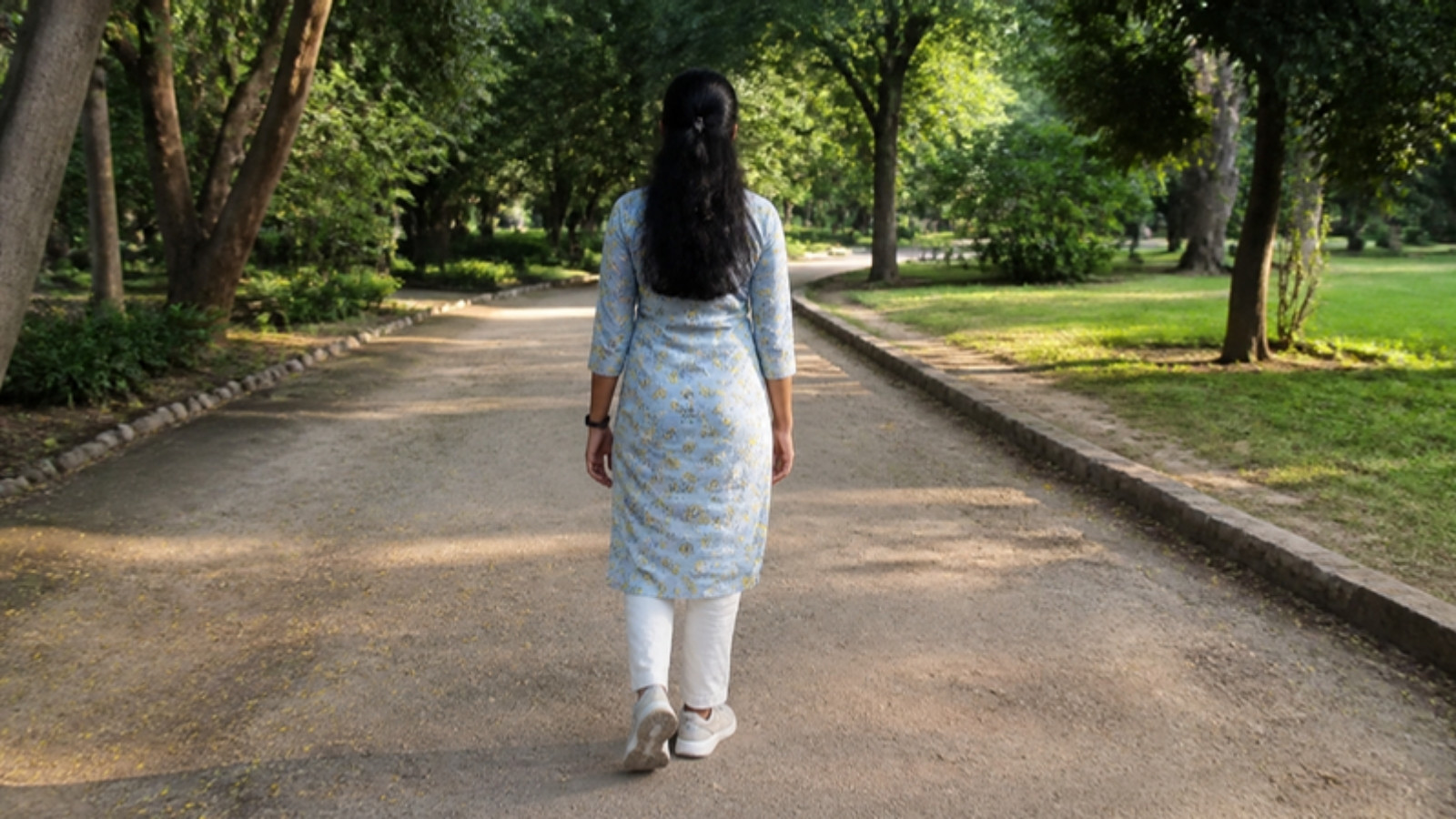 Woman in a kurta and sneakers walking on a tree-lined path