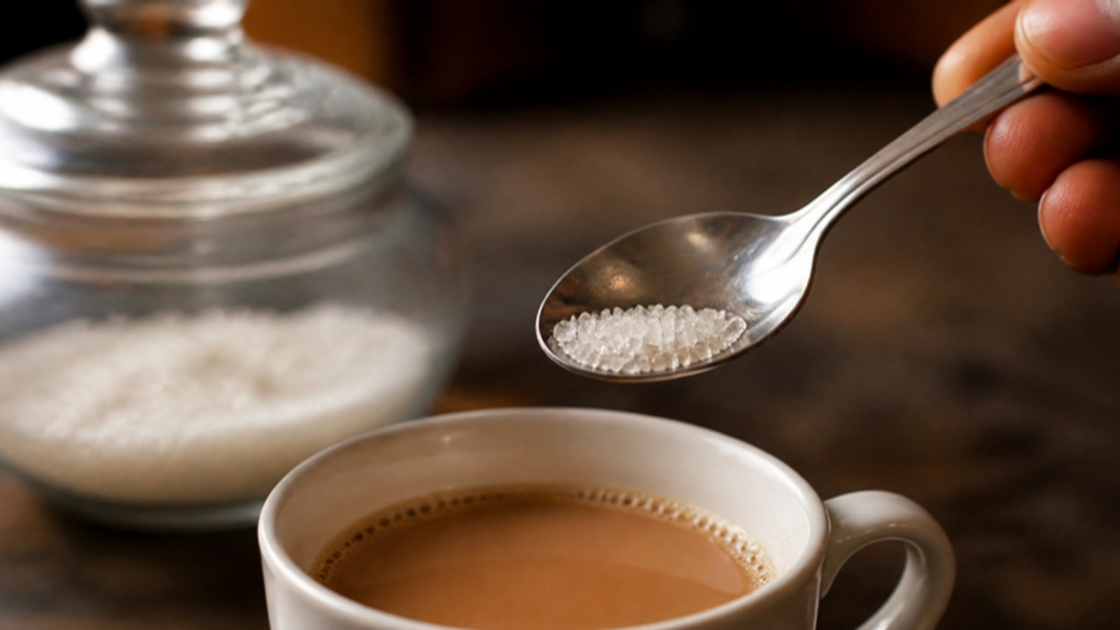 Teaspoon of sugar held over a cup of chai