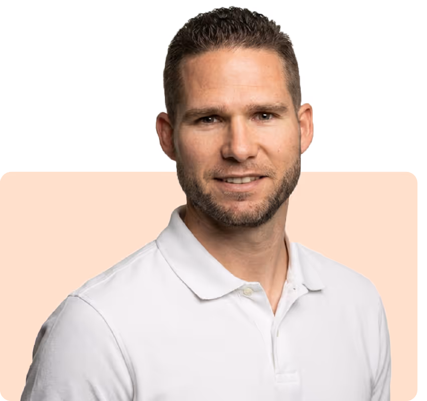 Smiling man with short hair and beard wearing a white polo shirt against a light peach background.