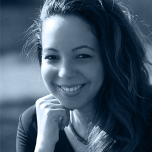 Smiling woman with long hair resting her chin on her hand in a close-up portrait.