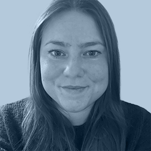Portrait of a woman with long hair smiling slightly against a plain blue background.