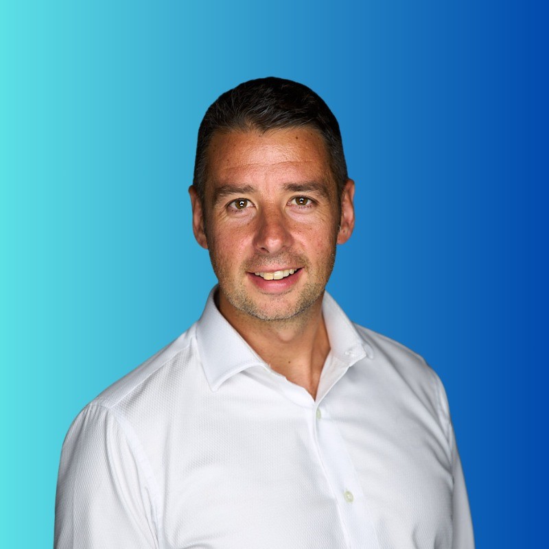 Man with short dark hair and light stubble wearing a white shirt on blue gradient background.