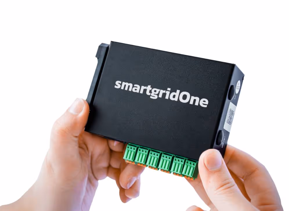 Hands holding a black smartgridOne device with green connectors against a white background.