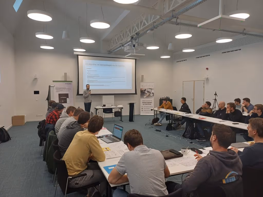 Man giving a presentation to a group seated around tables in a conference room with a projector screen.