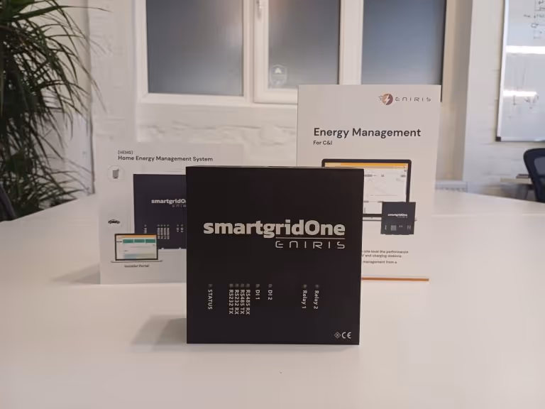 Black smartgridOne device by Eniris on a white table with Home Energy Management System brochures in the background.