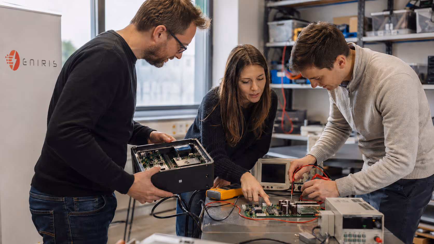 Three engineers examining and testing electronic circuit boards in a workshop.