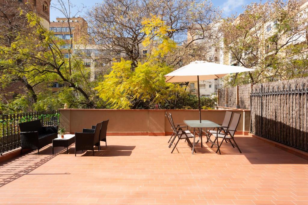 Outdoor terrace with terracotta tiles, featuring black wicker seating on the left and a glass table with four chairs and a white umbrella on the right.