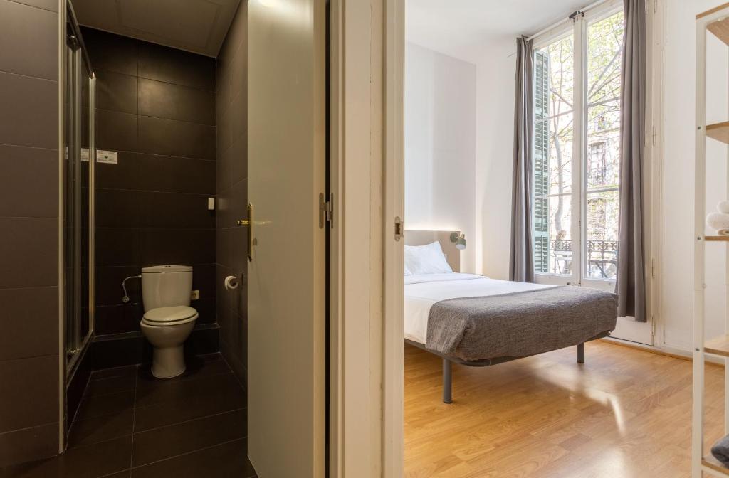 View showing modern bedroom with double bed and large window next to a bathroom with dark tiles and toilet.