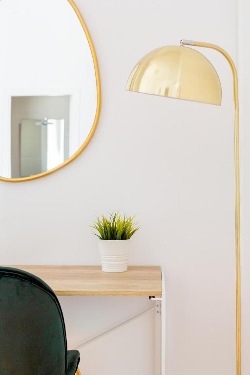 Minimalist workspace with a wooden desk, small potted plant, round wall mirror, gold floor lamp, and a dark green chair.