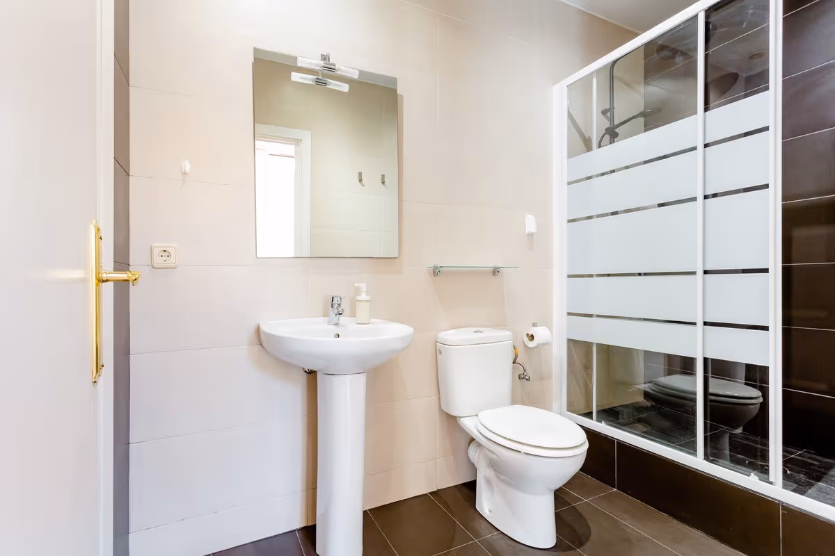 Modern bathroom with white pedestal sink, toilet, large mirror, and glass shower doors with frosted stripes.