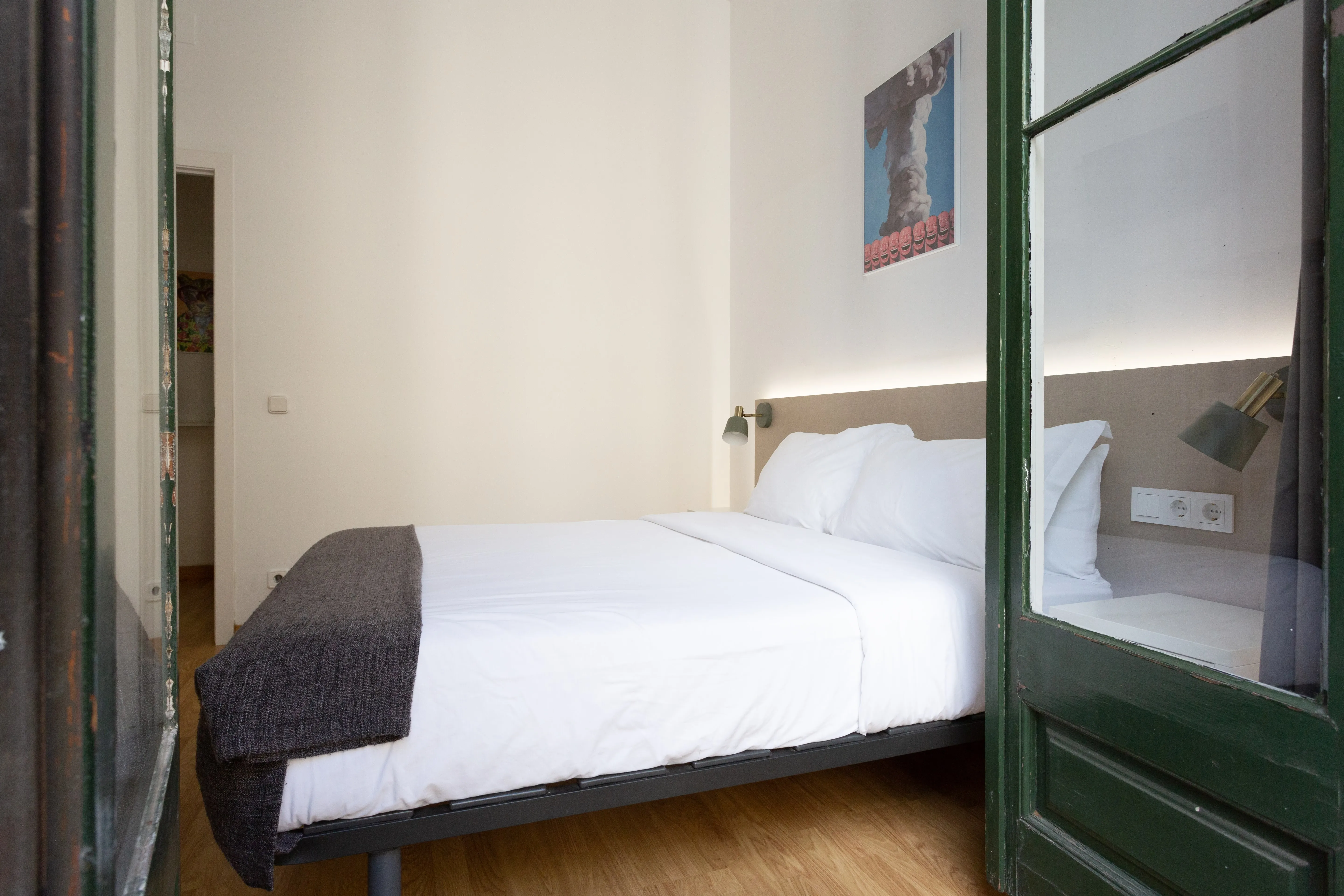 Minimalist bedroom with white bedding, gray blanket, wooden floor, and a small painting on the wall.