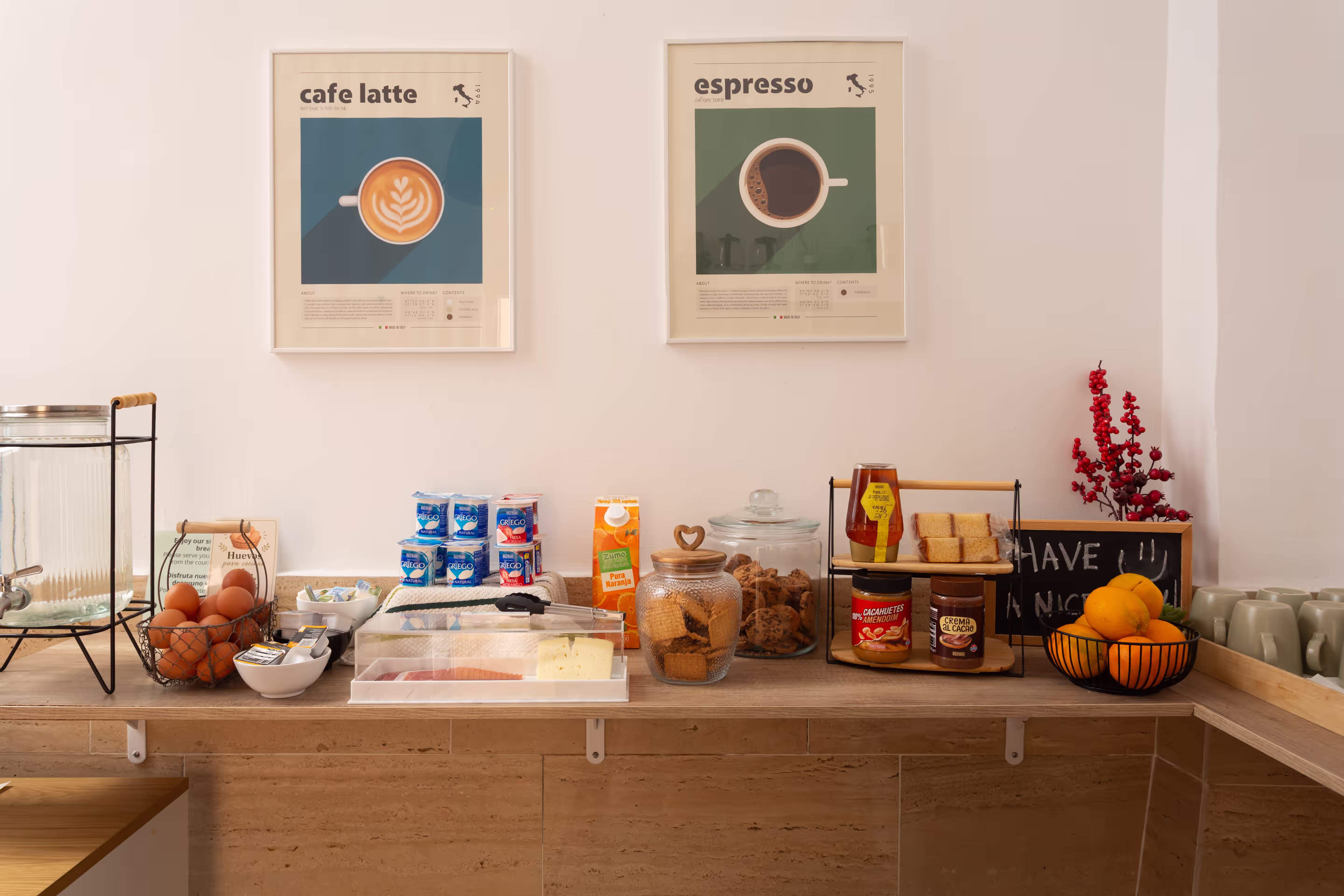 Counter with breakfast items including eggs, yogurt, juice, cookies, spreads, fruit, mugs, and coffee posters on the wall.