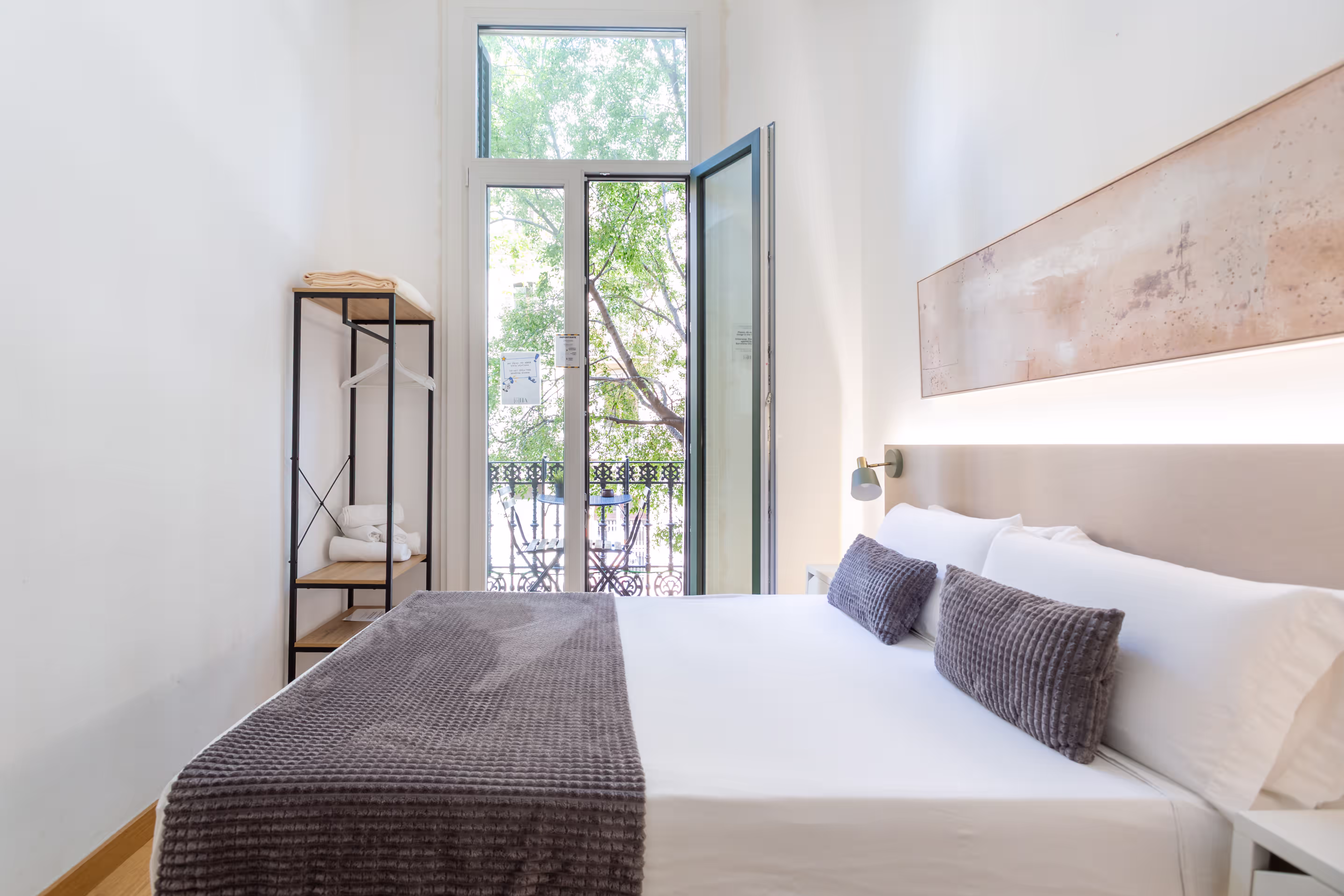 Bright bedroom with white walls, a large bed with gray pillows and blanket, an open balcony door.