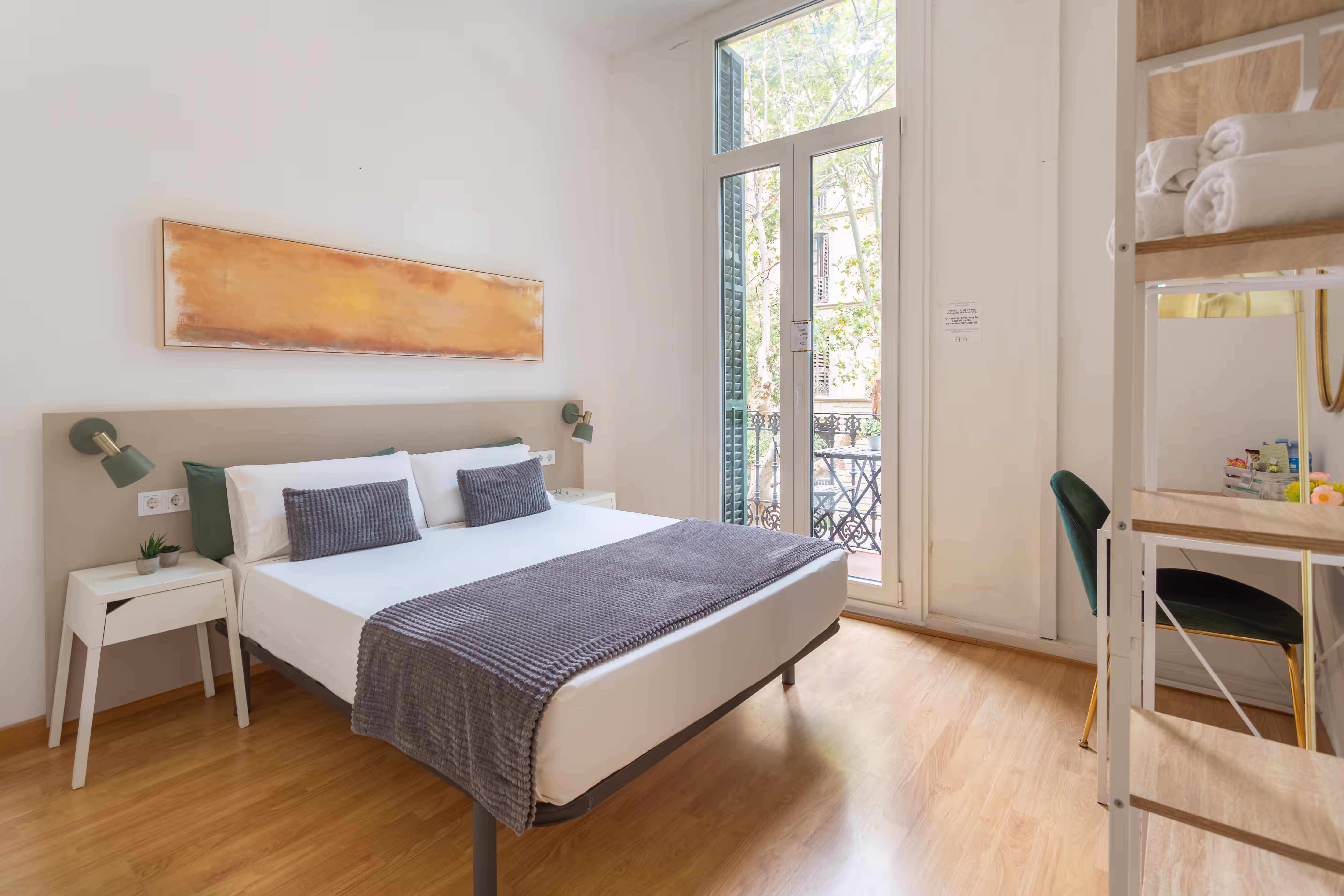 Bright bedroom with a double bed, gray throw and pillows, balcony door, and wooden floor.