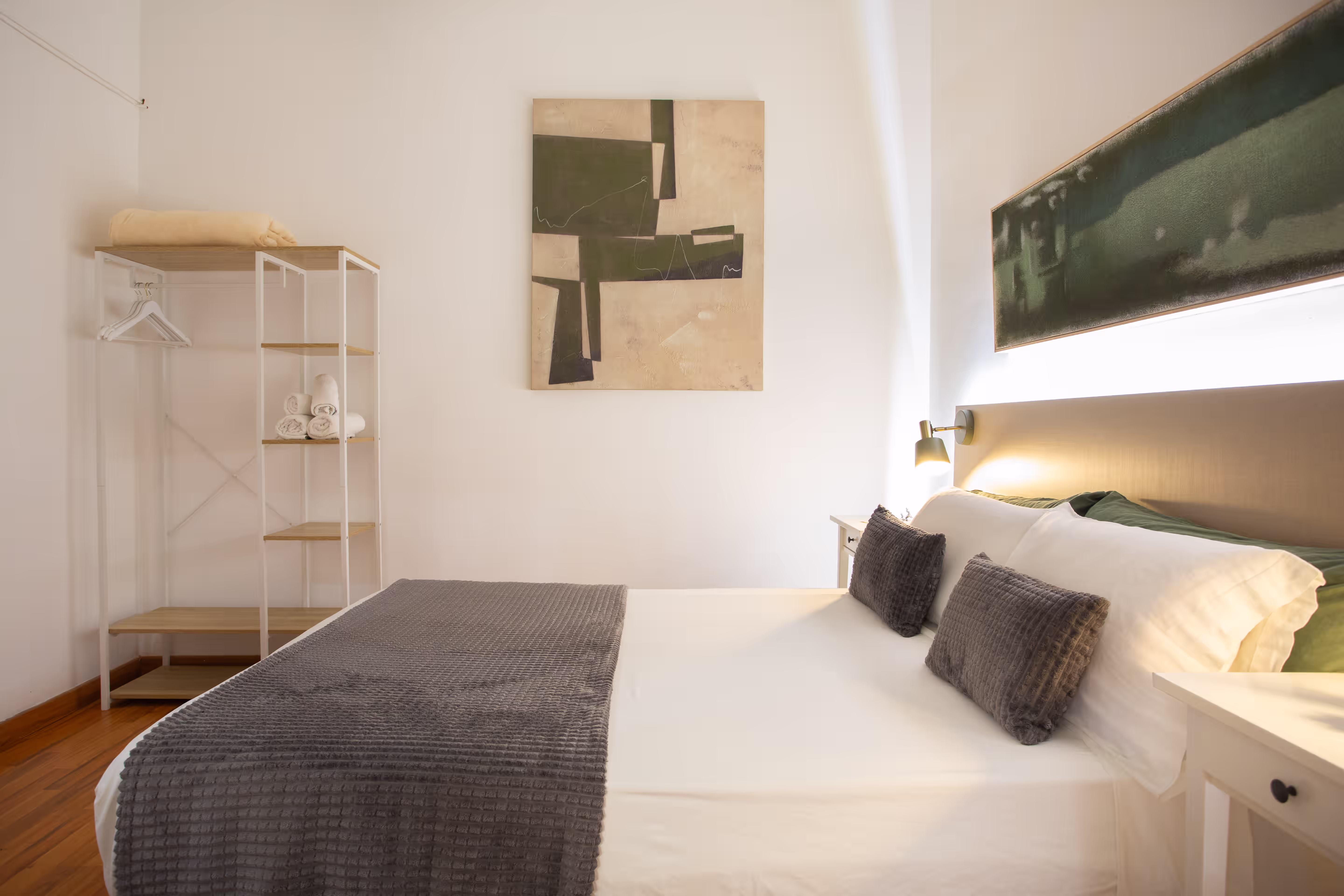 Modern bedroom with a neatly made bed, gray textured blanket, pillows, and abstract wall art.
