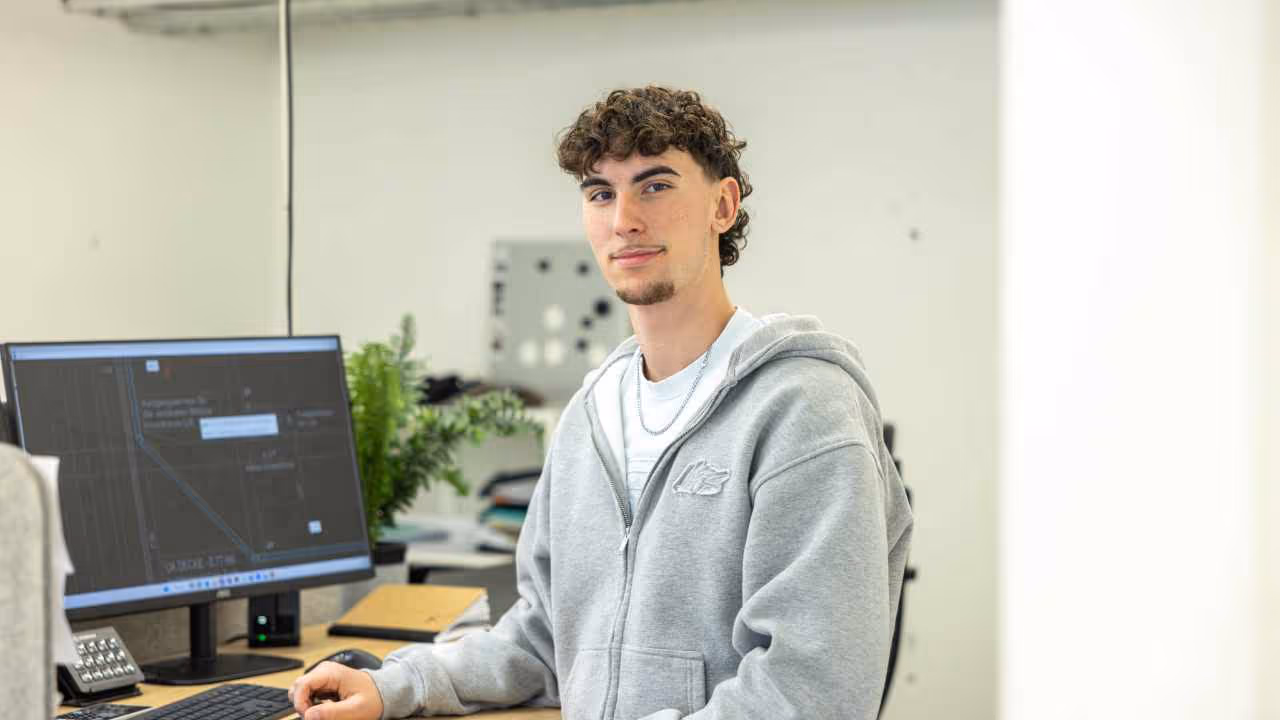 Auszubildender oder junger Mitarbeiter am PC-Arbeitsplatz mit CAD-Software, modernes Bürodesign und helle Arbeitsumgebung.