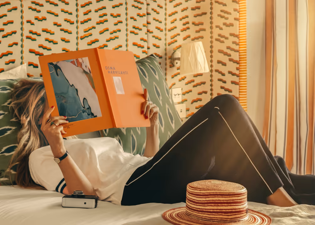 Pause lecture aux Cimes Bleues : détendez-vous dans les chambres et suites design de votre hôtel au bord de mer et hôtel spa, livre orange à la main.