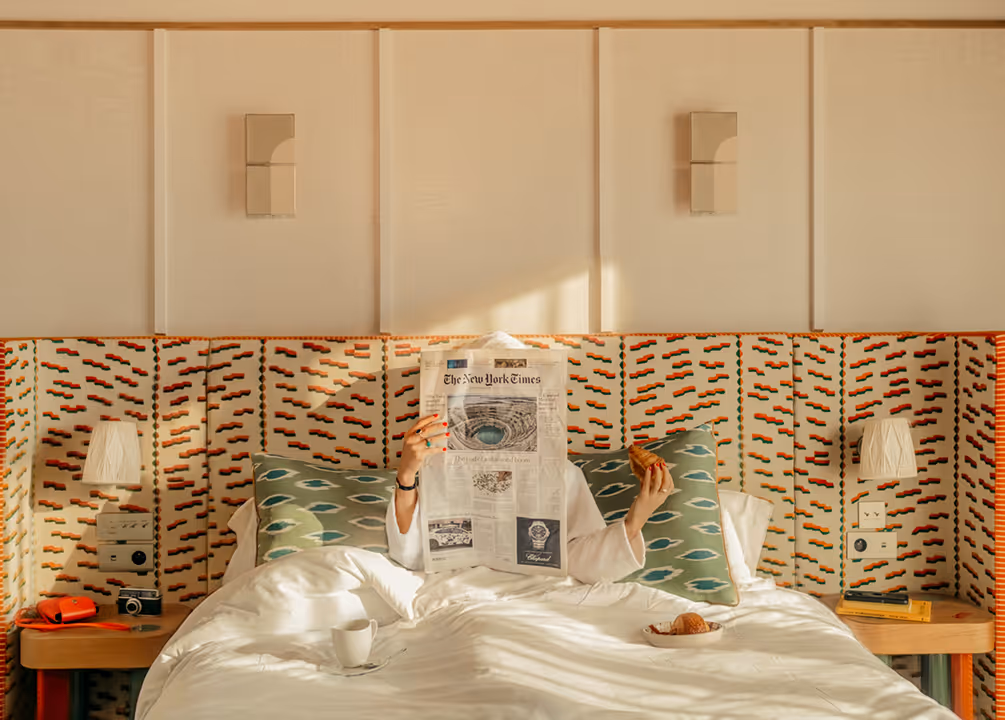 Matinée douce aux Cimes Bleues : une personne lit le journal et savoure un croissant au lit, nichée au cœur des chambres et suites de votre hôtel au bord de mer et hôtel spa.