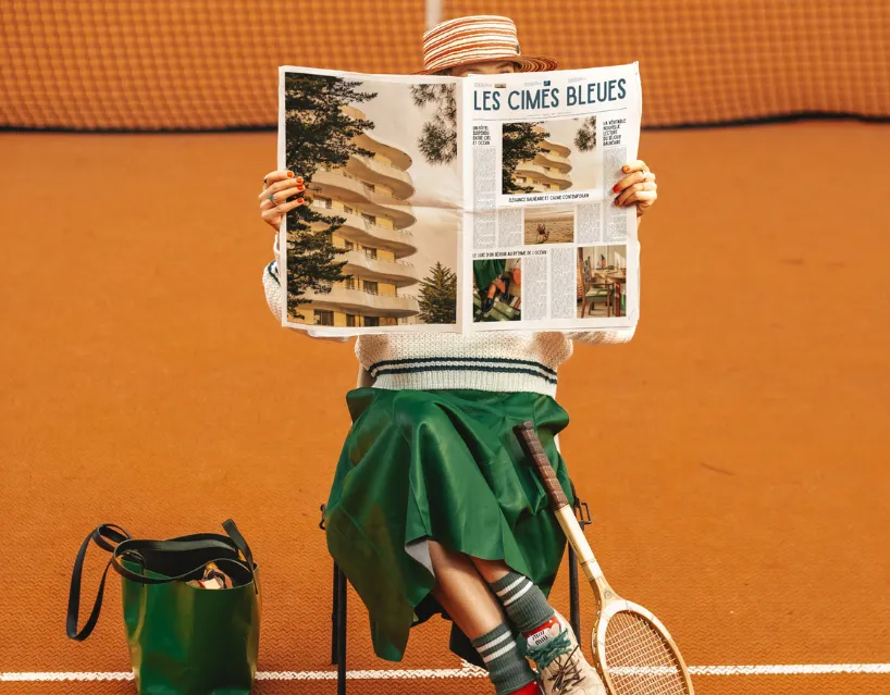 Femme chic lisant le journal sur un court de tennis aux Cimes Bleues, votre hôtel au bord de mer et hôtel spa parfait pour l'organisation de séminaires.