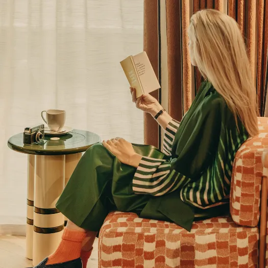 Femme lisant un livre dans un fauteuil design aux tons terracotta, moment de détente raffiné dans une chambre des Cimes Bleues à La Baule.