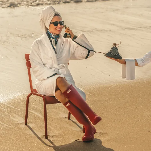 Woman in a white bathrobe calling on a vintage handset from La Baule beach, reflecting the chic service and humor of Les Cimes Bleues.