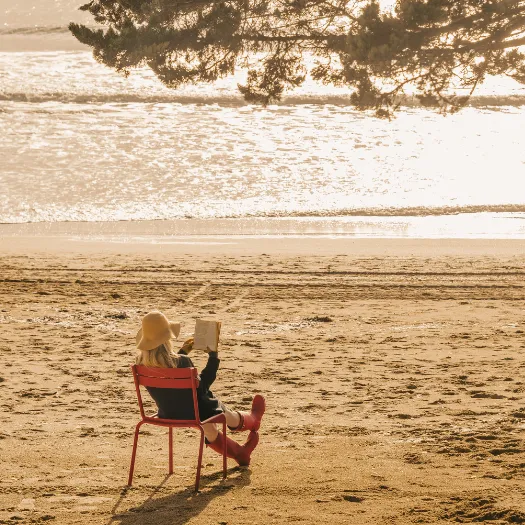 A woman reading a book on La Baule beach at sunset, a moment of serenity and dolce vita in the spirit of Les Cimes Bleues.