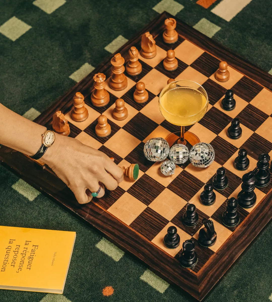 Gros plan sur une partie d'échecs avec cocktail et boules à facettes sur l'échiquier, ambiance bar chic et décalée au bar des Cimes Bleues à La Baule.