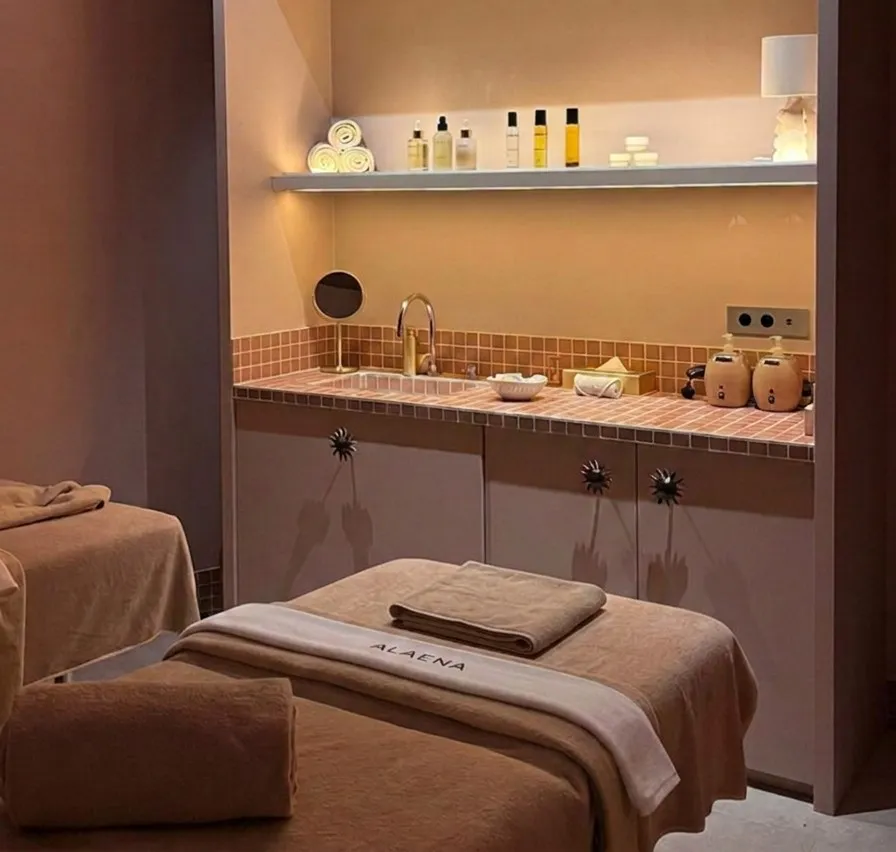 Tables de massage du spa Alaena avec des serviettes et des produits de soins posés sur une étagère.