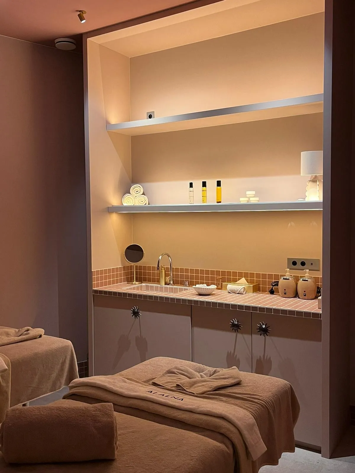 Alaena des Cimes Bleues spa massage table with skincare products on a shelf.