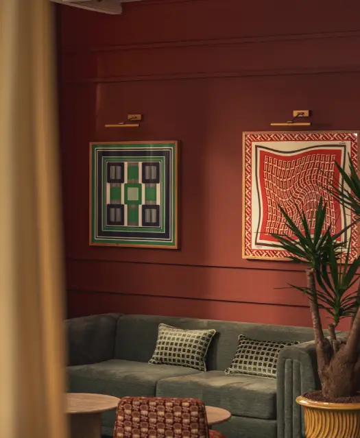 Espace commun de l'hôtel Les Cimes Bleues, avec deux tableaux, un canapé, une plante et deux tables basses, aux teintes chaleureuses entre terre et mer. 