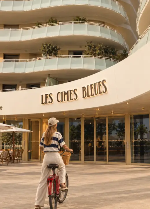 Façade l'hôtel Les Cimes Bleues avec de la végétation et un vélo rouge à l'entrée. 
