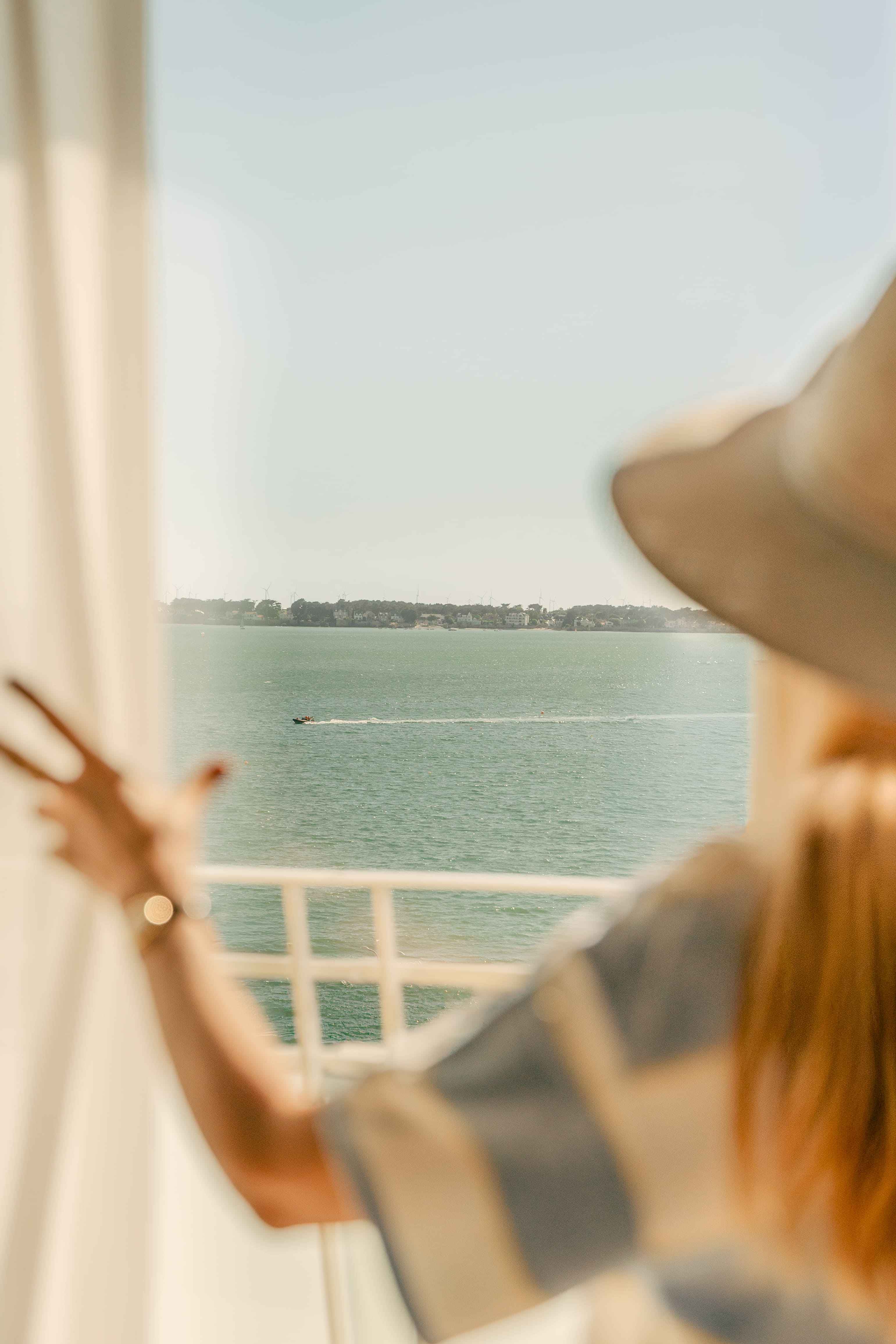 Femme avec un chapeau admirant une vue sur l'océan depuis le balcon de sa chambre.
