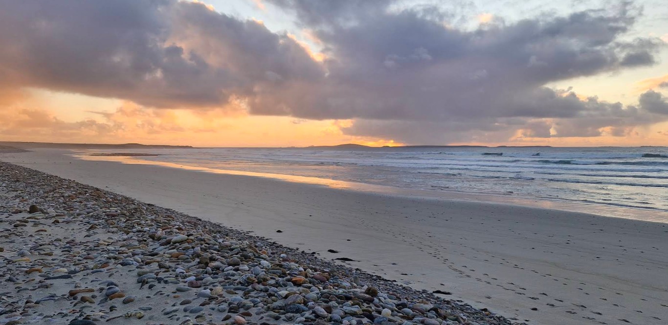 Rocky beach with waves gently crashing under a cloudy sky at sunset.
