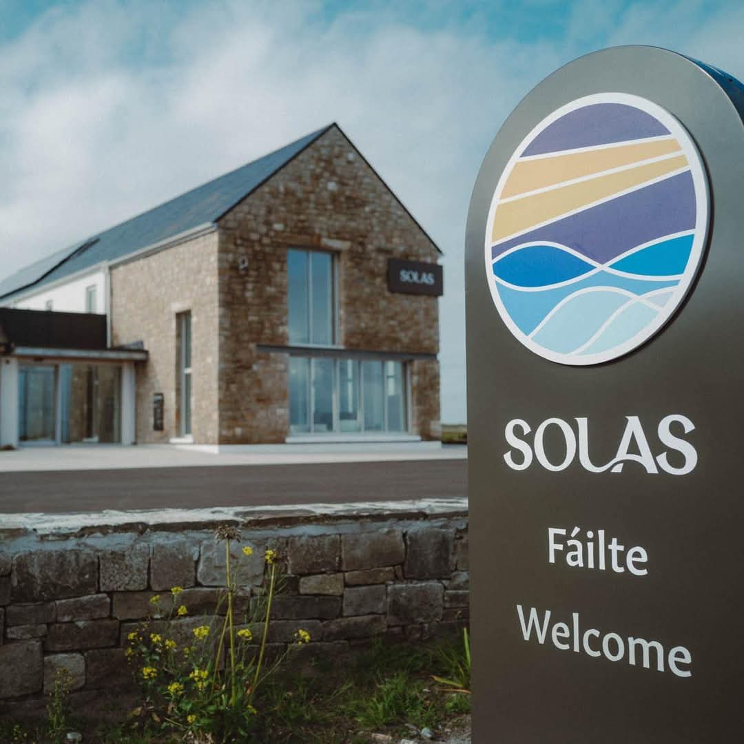 Stone building with solar panels in the background and a sign reading 'SOLAS Fáilte Welcome' in the foreground.