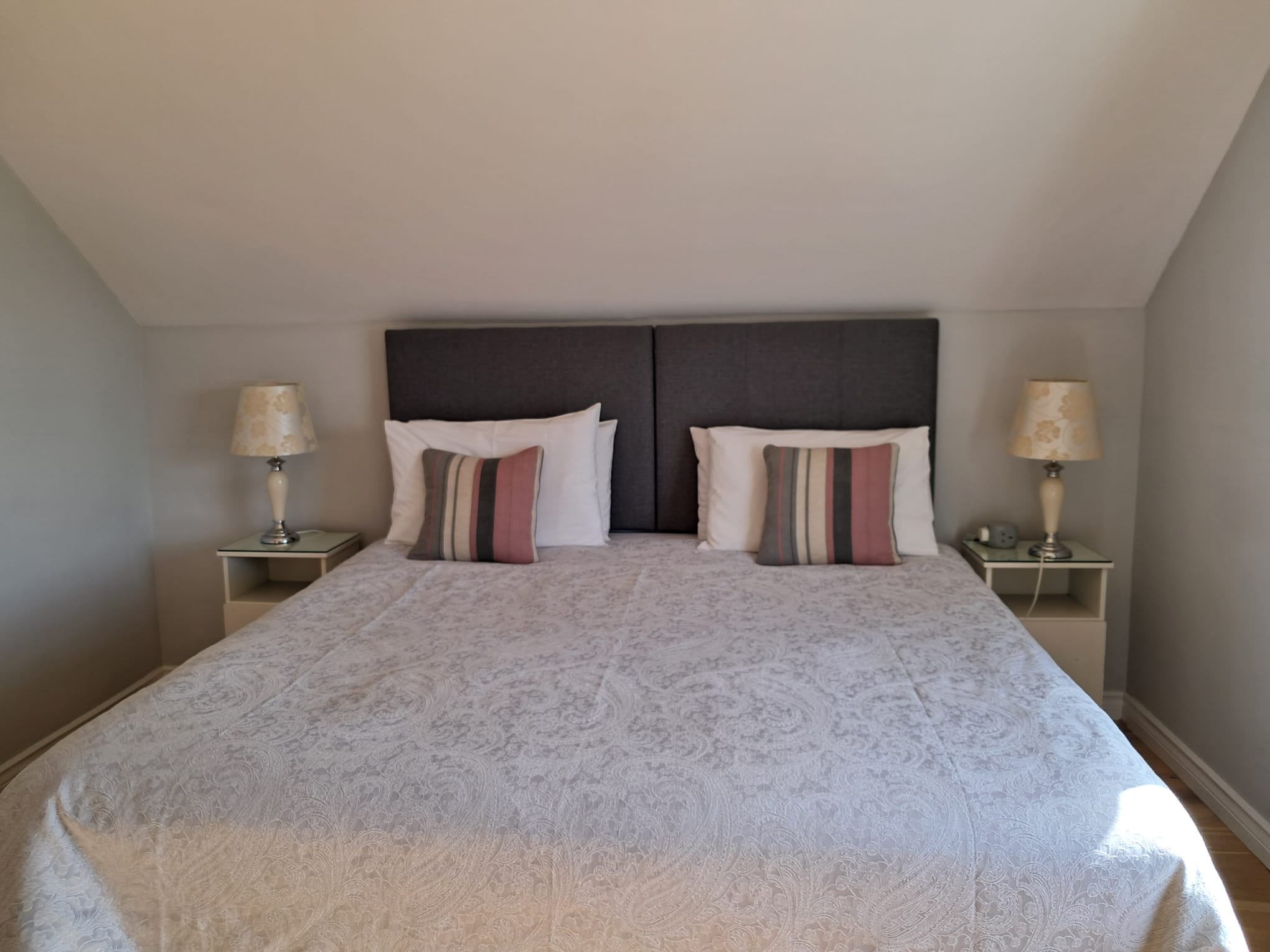 Double bed with gray headboard, white and striped pillows, floral lamps on mirrored bedside tables.