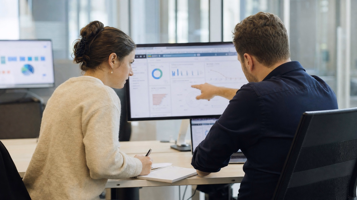 Colleagues review cloud data on shared screen, one taking notes