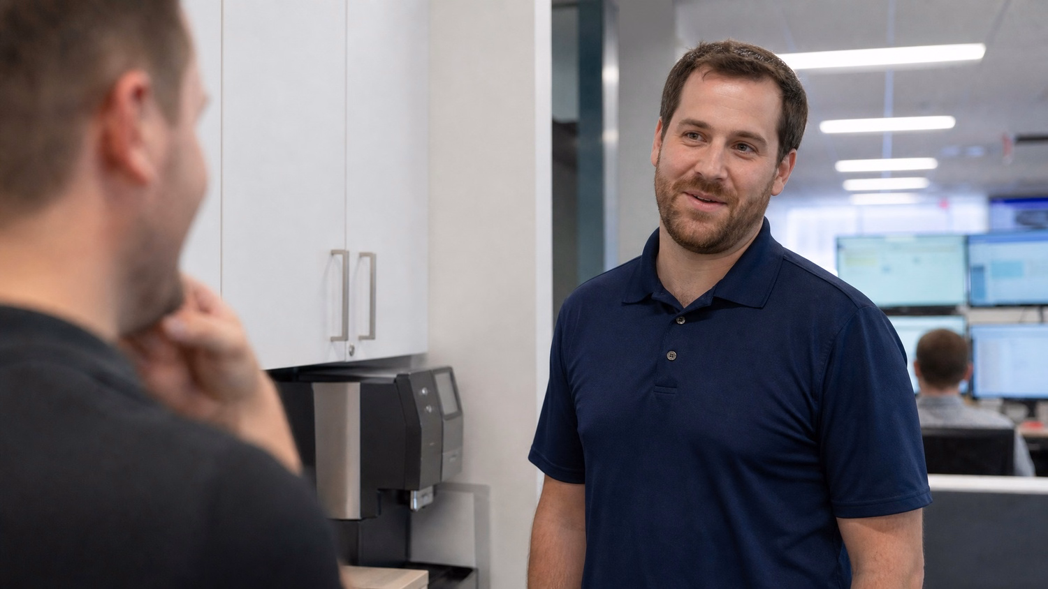 Colleague chats near coffee machine, navy polo shirt 58 chars
