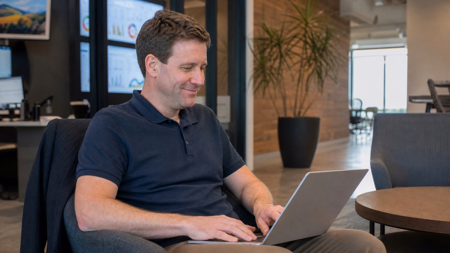 Man in navy polo reviews laptop in office lounge area