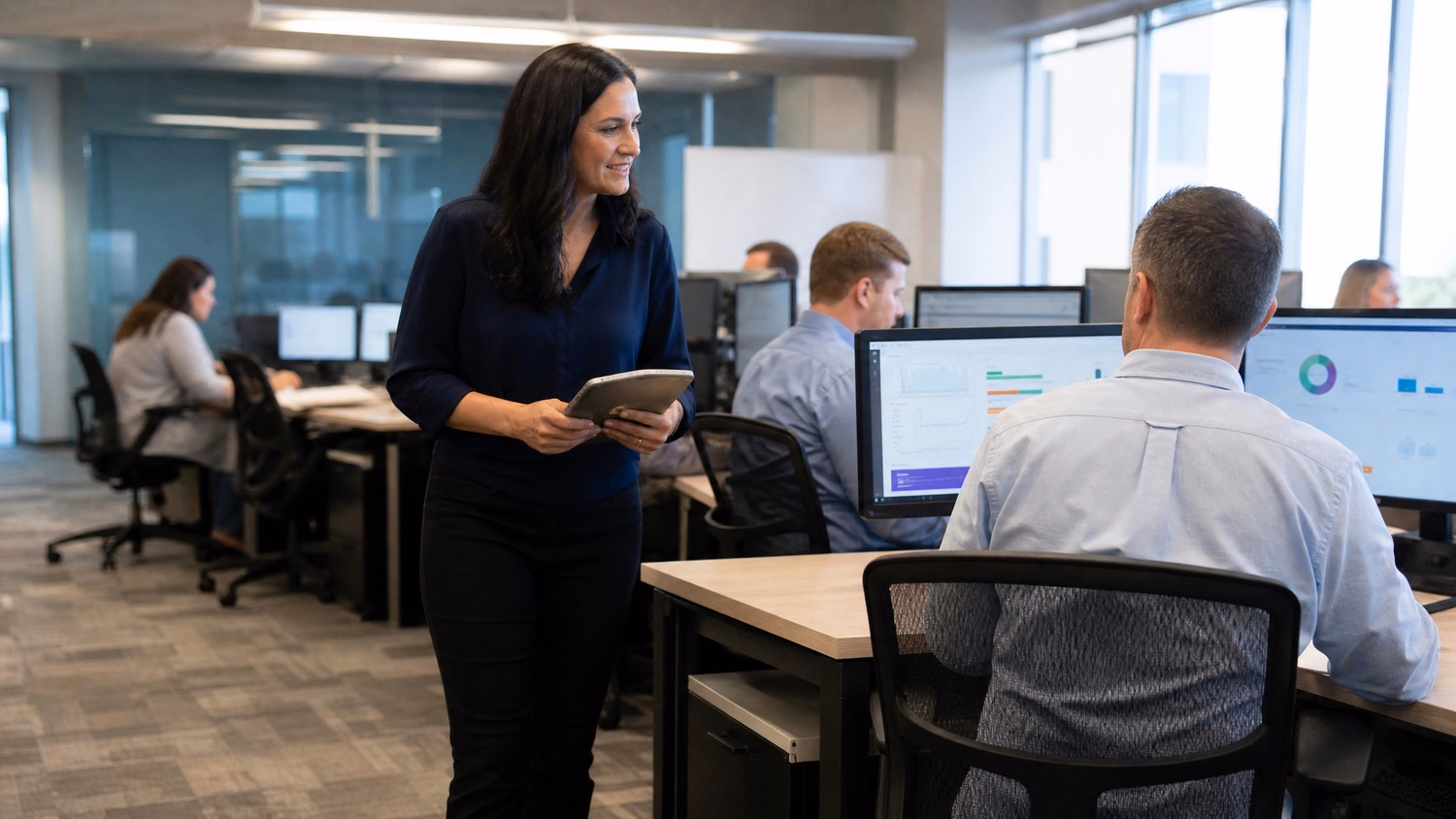 Woman walks through office reviewing data on monitor