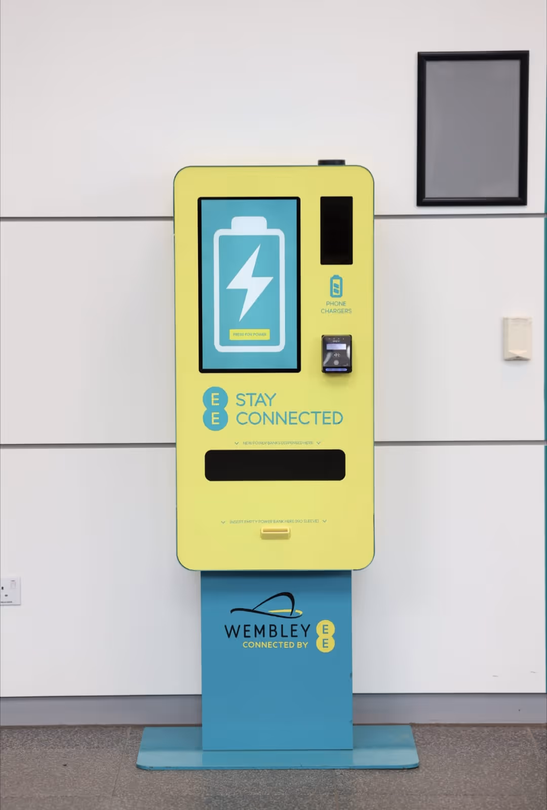 Bright yellow and blue phone charging station with a battery icon and text 'Stay Connected' and 'Wembley Connected by EE'.