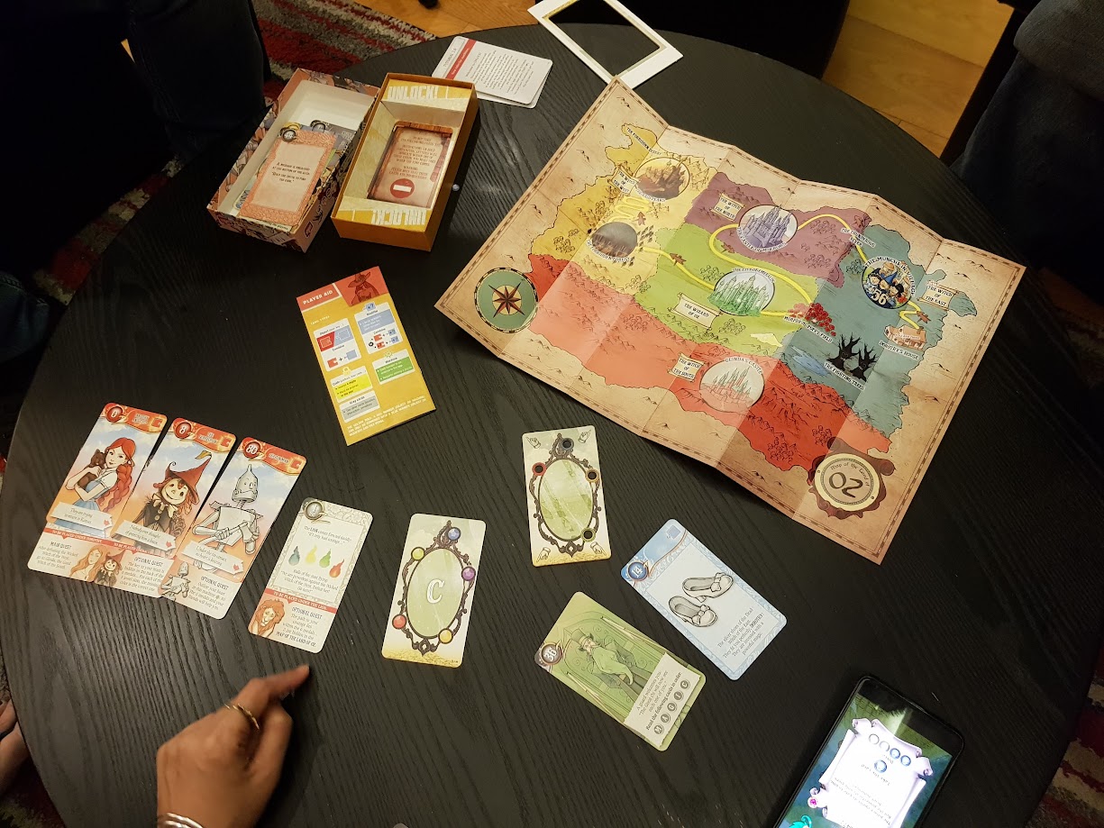 Gameplay photo of the board game Unlock!: Secret Adventures – The Adventurers of Oz featuring various components and board state.
