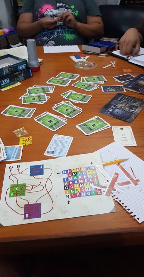 Gameplay photo of the board game EXIT: The Game – The Abandoned Cabin featuring various components and board state.