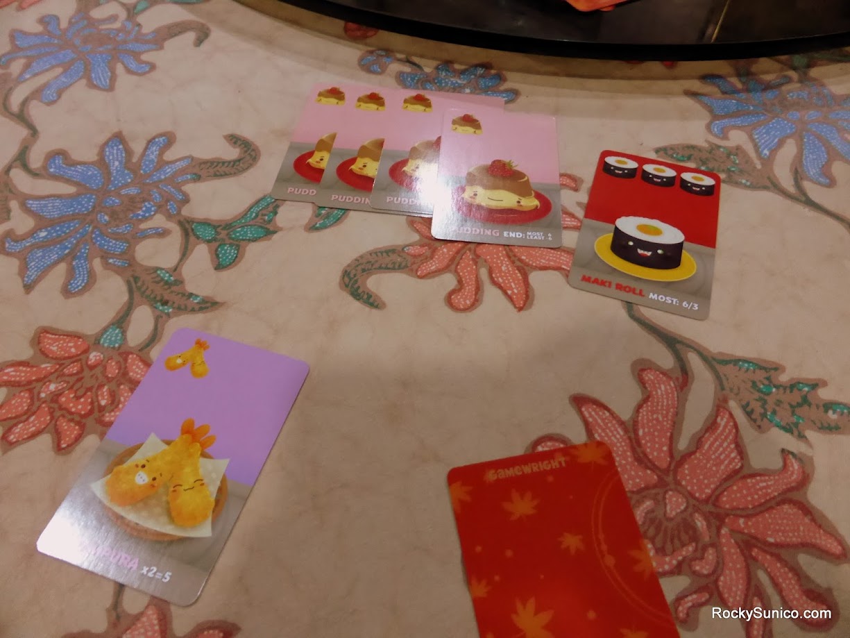 Gameplay photo of the board game Sushi Go! featuring various components and board state.
