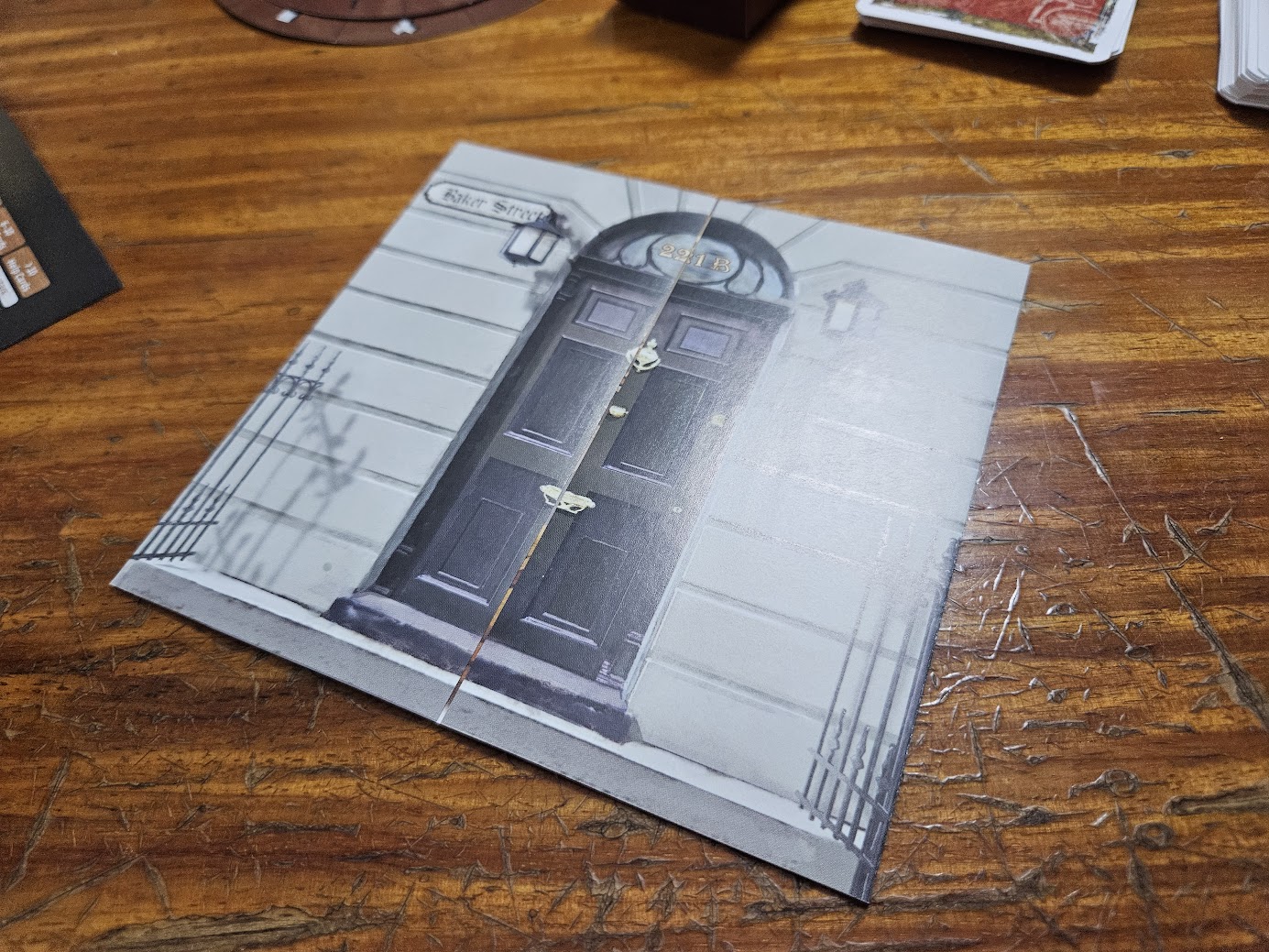 Gameplay photo of the board game EXIT: The Game – The Disappearance of Sherlock Holmes featuring various components and board state.